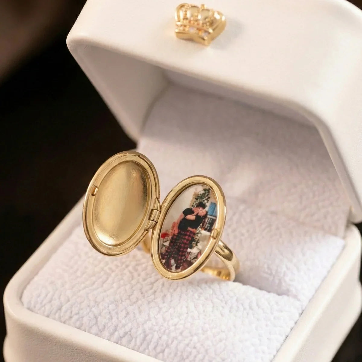 Gold oval locket ring shown open in a white ring box, with a photo displayed inside.